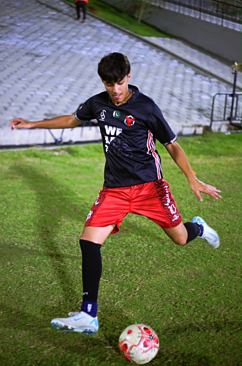 Zavyan Haider controlling the ball in a black kit during a night match